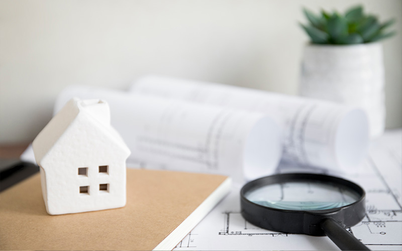 Miniature house with blueprints for property sales.