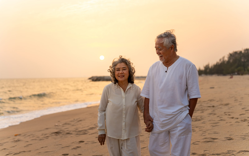 CKS elderly couple enjoying retirement on a beach at sunset.